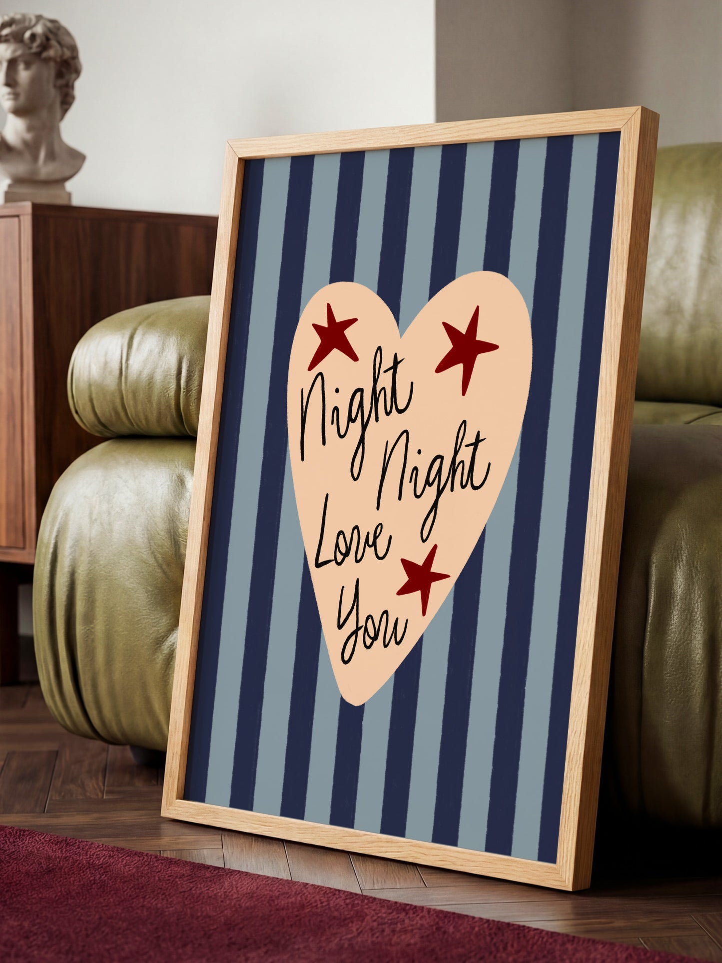 A framed poster with a heart-shaped design and text on it, placed on a wooden floor in a room with a couch and a statue.
