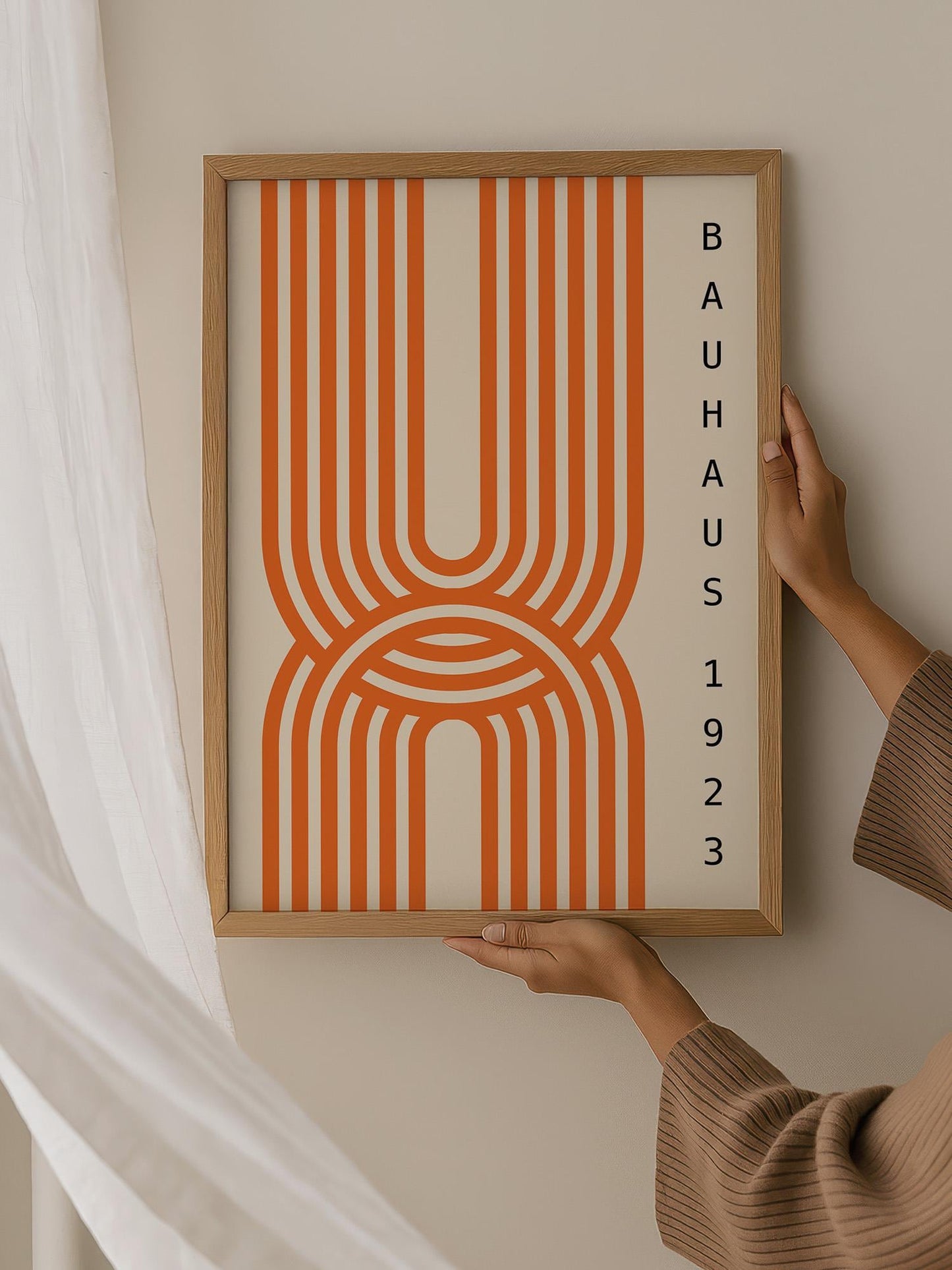 A person is holding up a framed poster with a bold, abstract design featuring orange and white stripes.