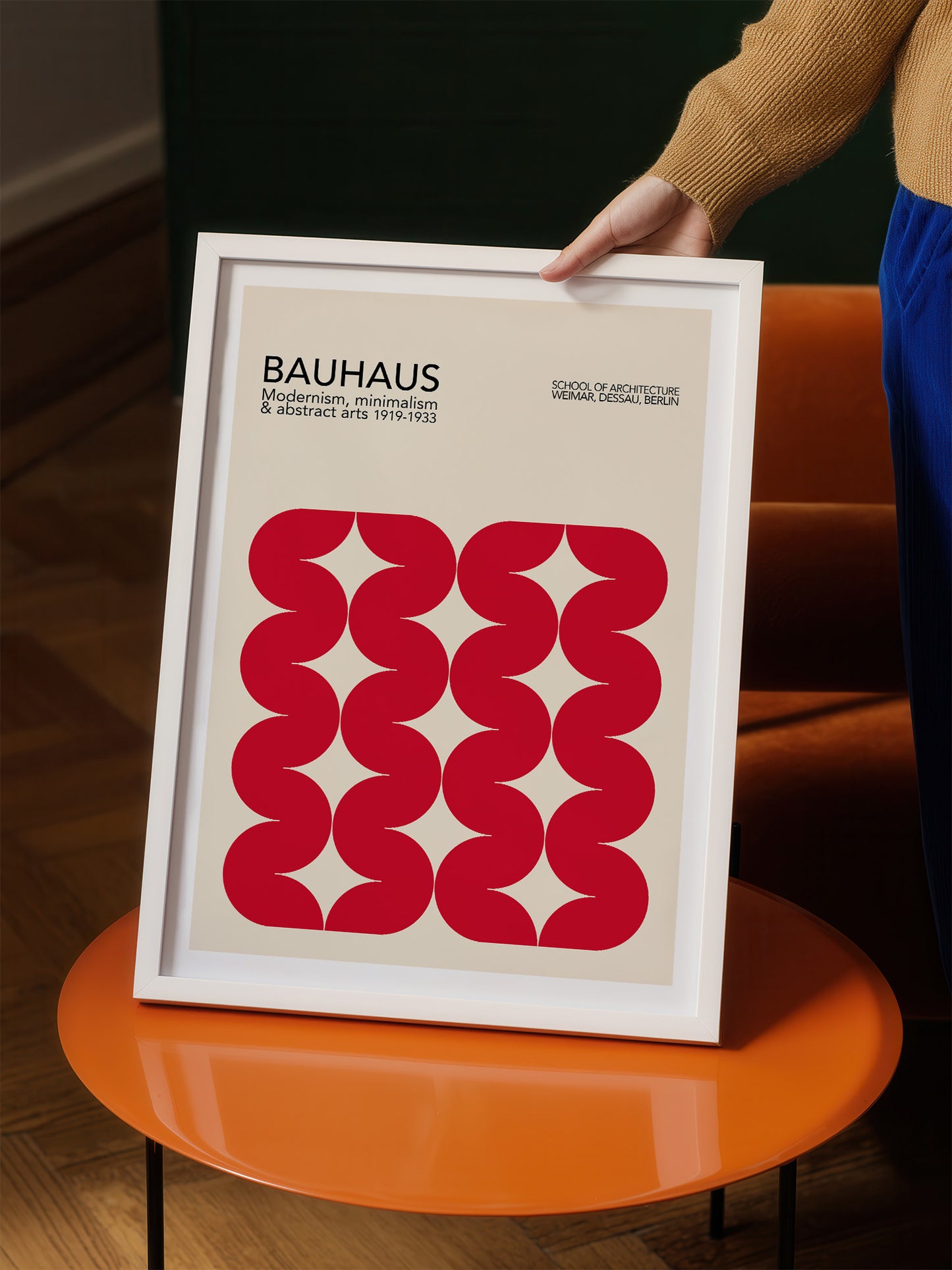A person is holding a framed poster with a minimalist design featuring a repeating pattern of red circles on a beige background.