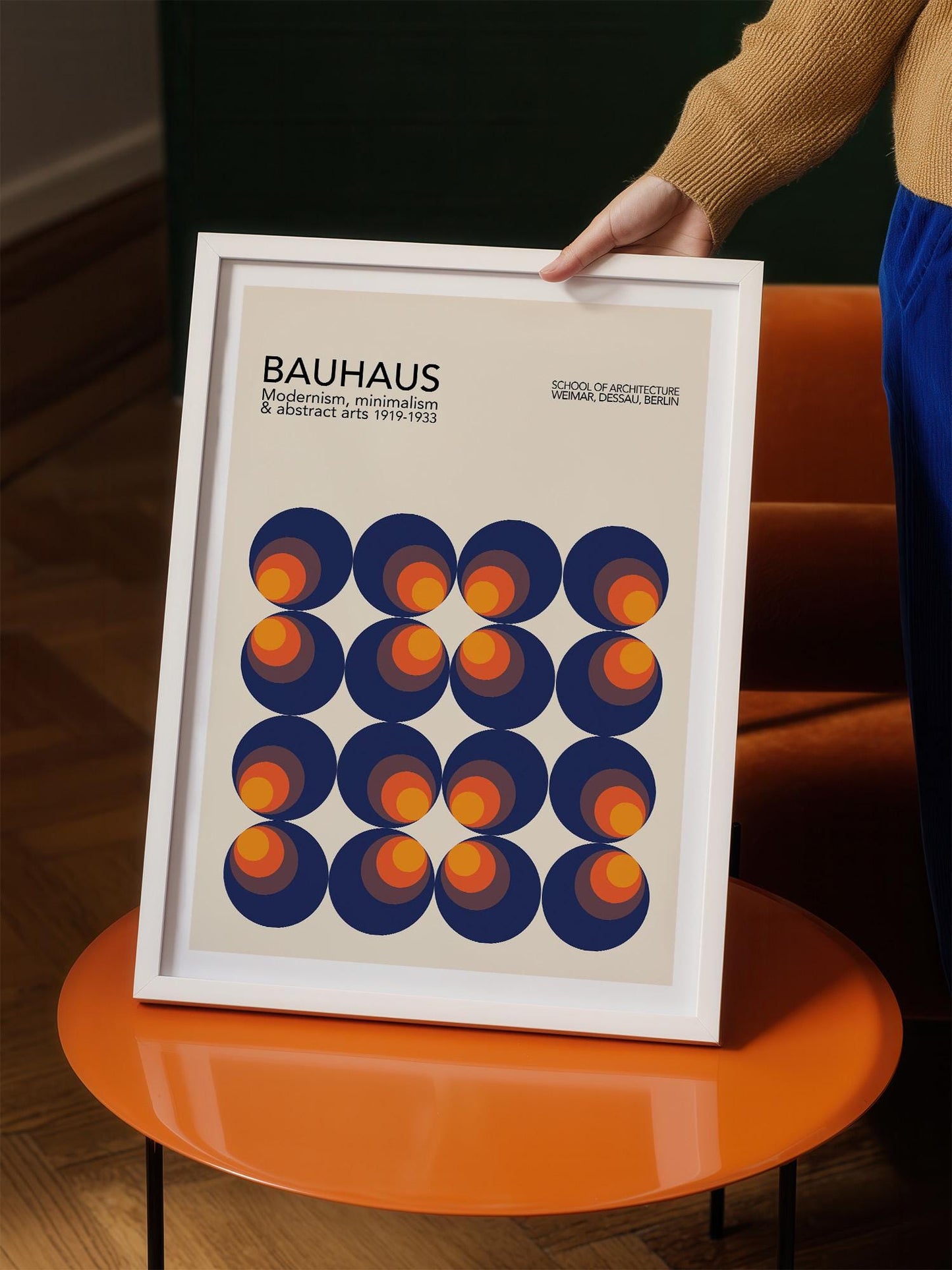 A person is holding a framed poster with a geometric design featuring circles in various shades of blue, orange, and yellow.
