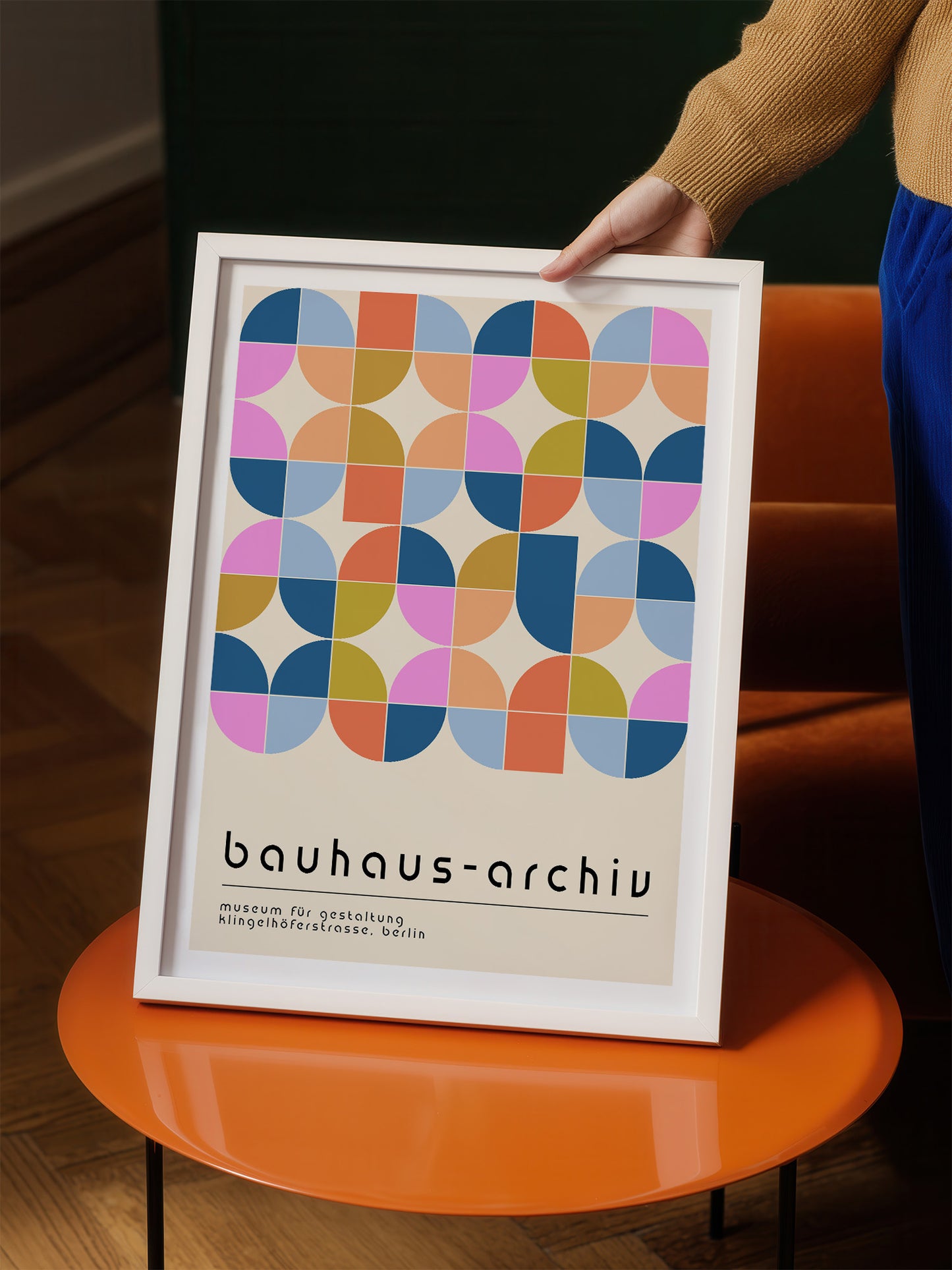 A person is holding a framed poster with a geometric design featuring circles and squares in various colors.