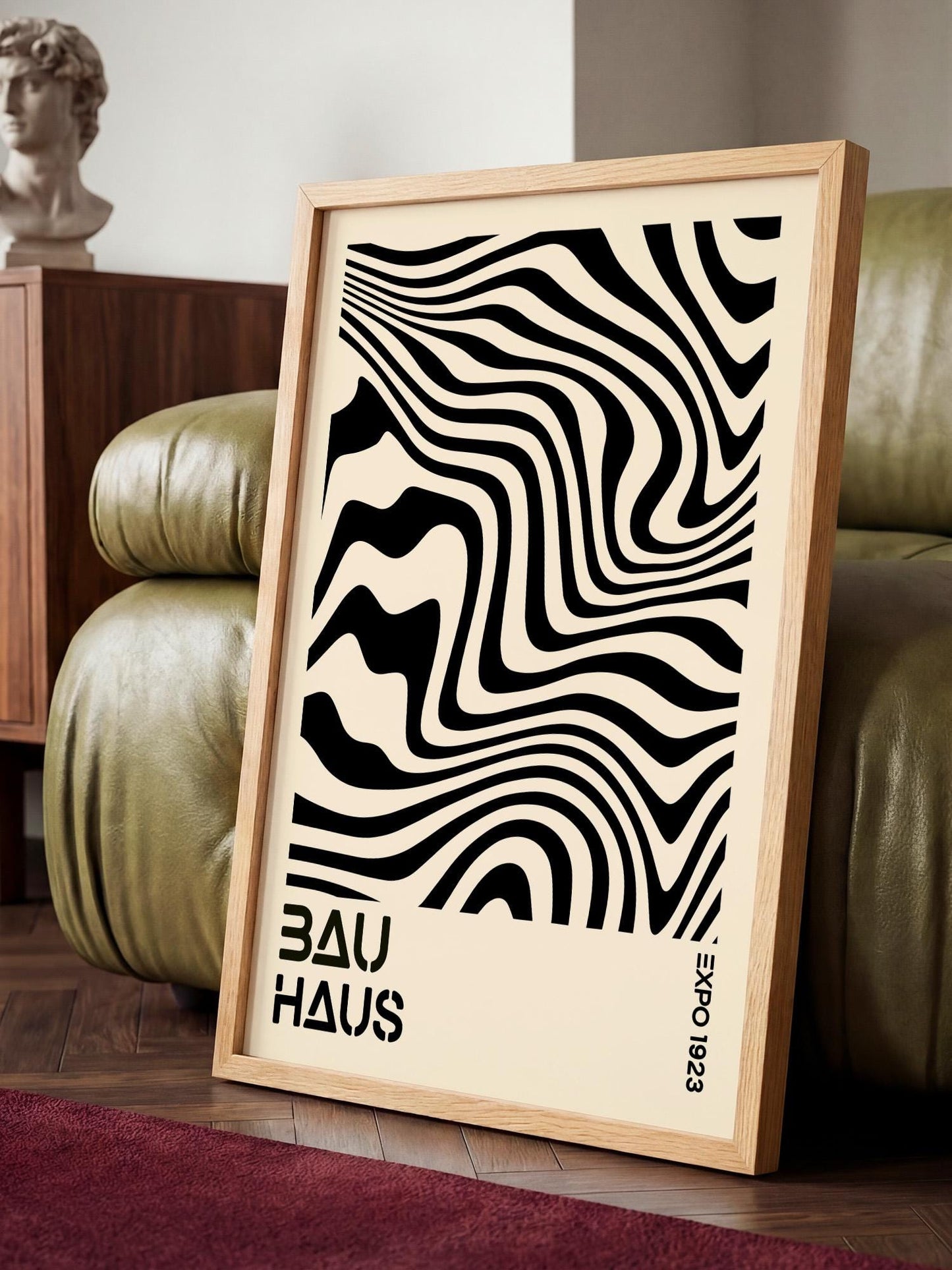 a framed poster with a striking black and white abstract design, placed on a wooden floor in a room with a green leather couch.