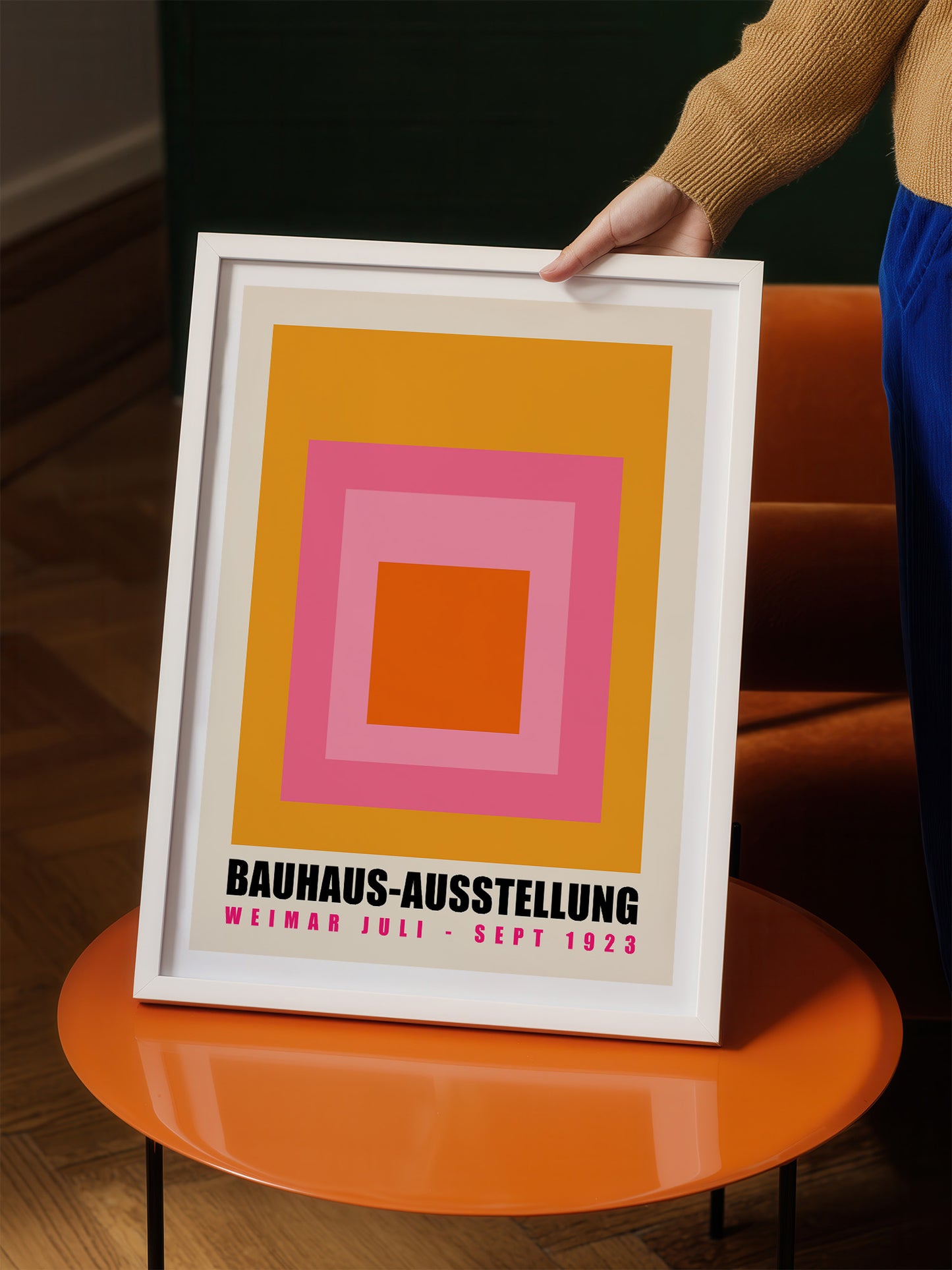 A person is holding up a framed poster with a bold geometric design in shades of pink, orange, and yellow.