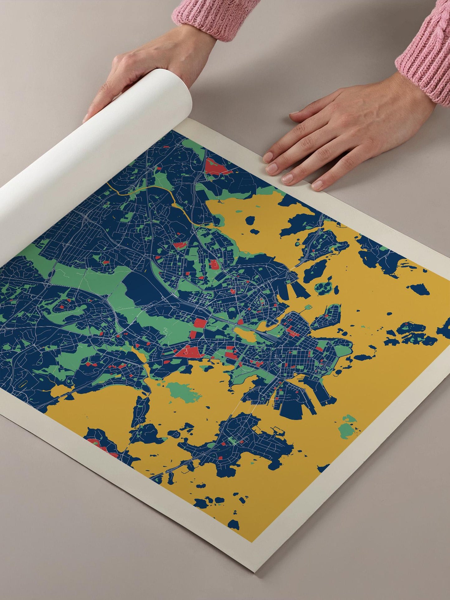 A person's hands are holding a roll of paper over a colorful map of a city, which appears to be a detailed and vibrant representation of the urban landscape.