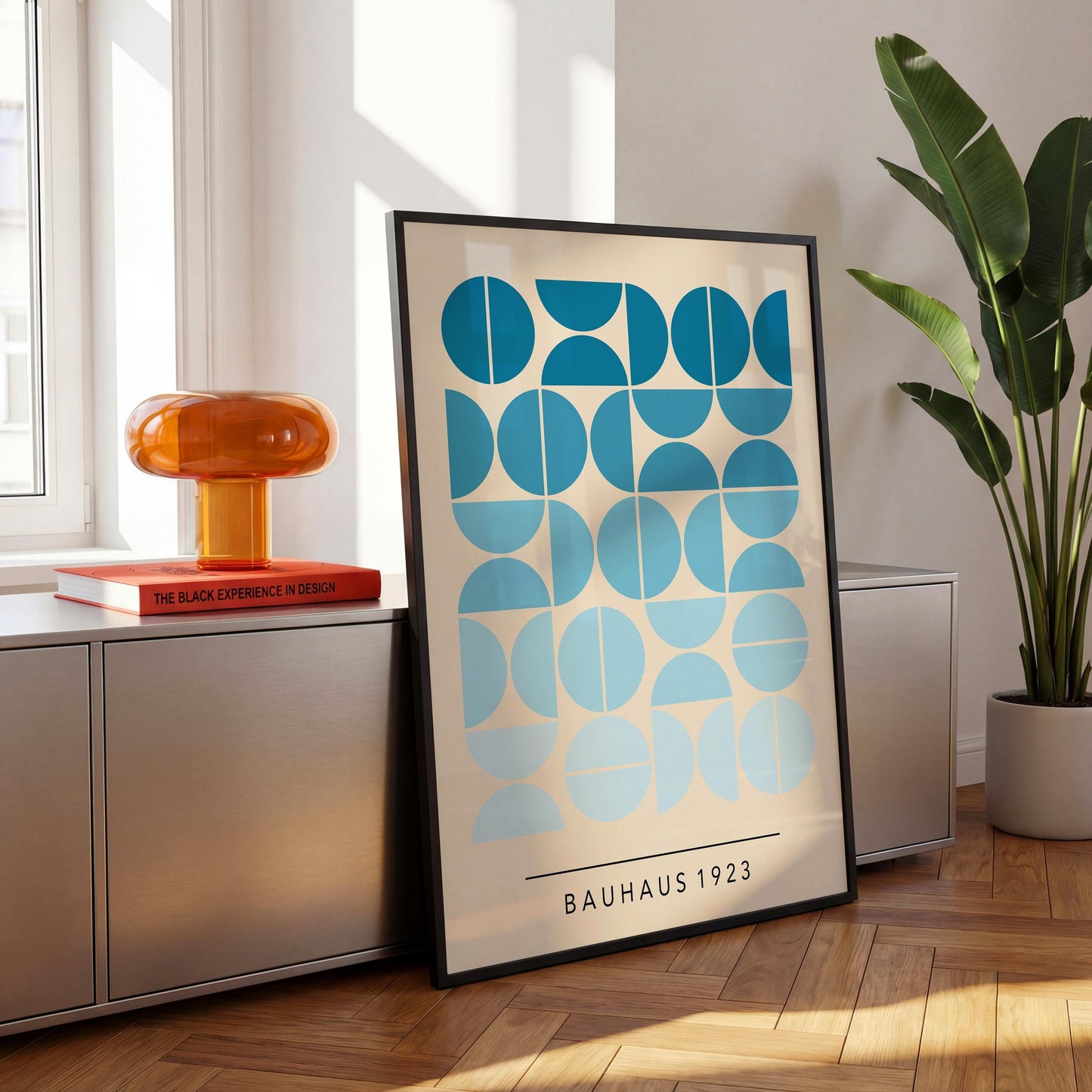 a large abstract art poster with a geometric design in shades of blue and white, displayed on a wooden floor next to a potted plant and a red lamp.