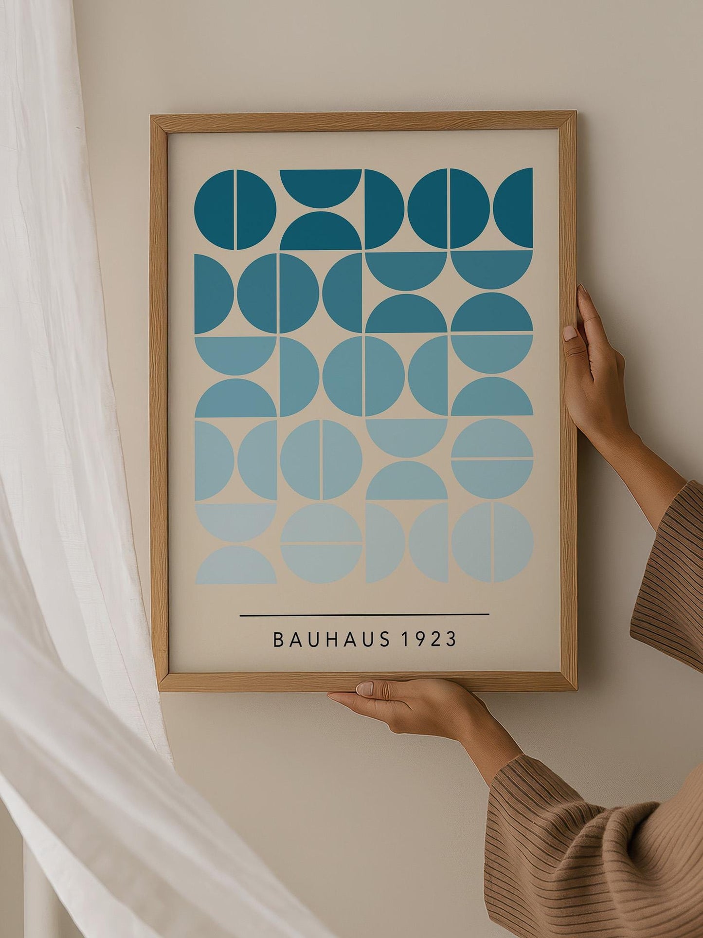 A person is holding up a framed print with a geometric design in shades of blue and white.