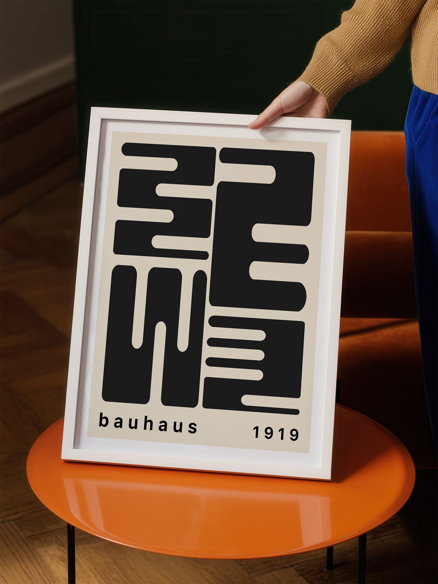 A person is holding a framed poster with a minimalist design featuring bold black shapes and text.