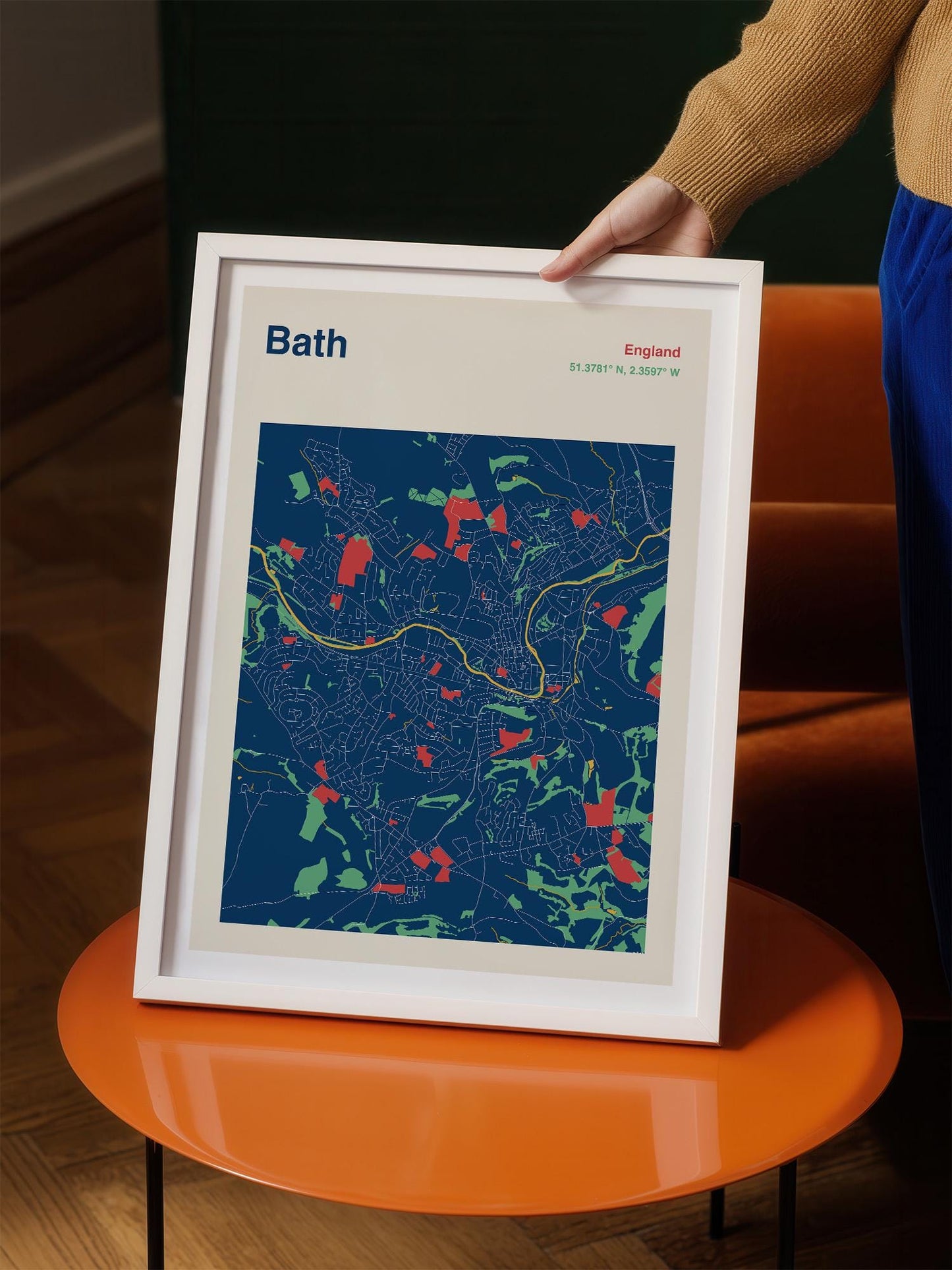 A person is holding a framed map of Bath, England, with a colorful and detailed map of the city displayed on the frame.