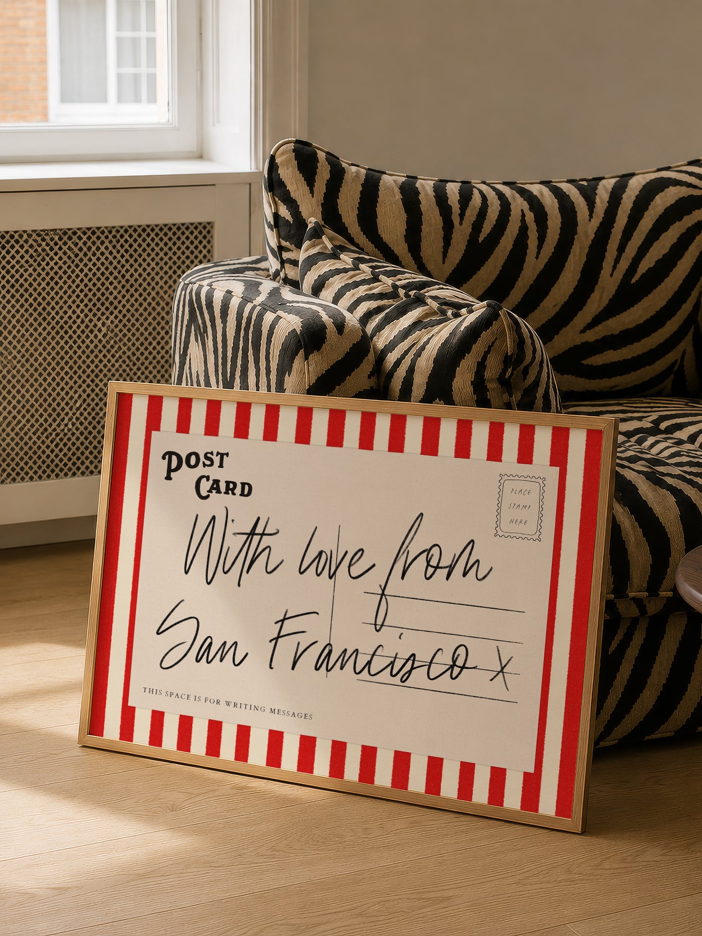 A framed postcard with a handwritten message is placed on a couch in a room with a window.