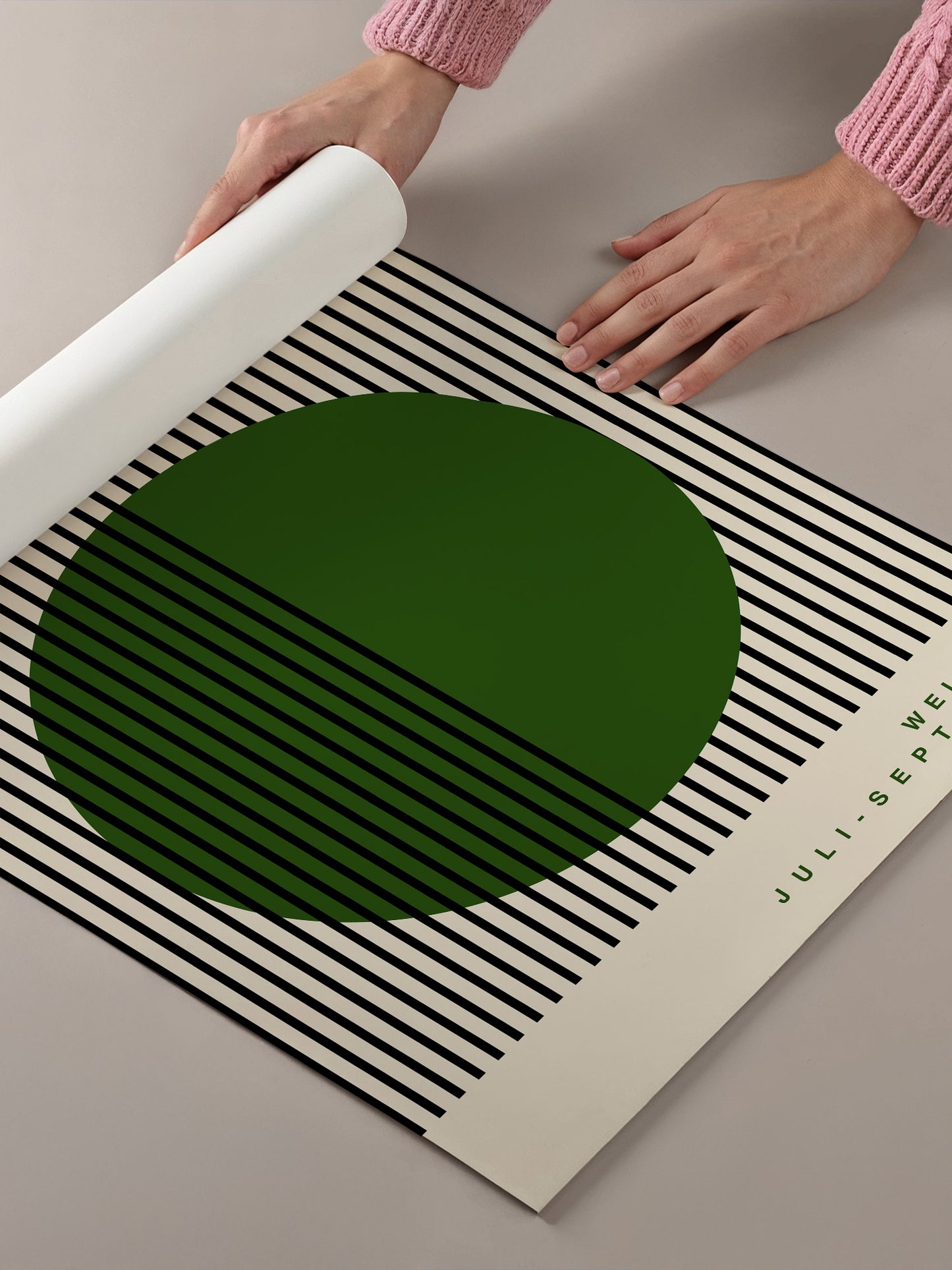 A person's hands are holding a roll of paper, which appears to be a large piece of paper with a green circle and black and white striped pattern on it.