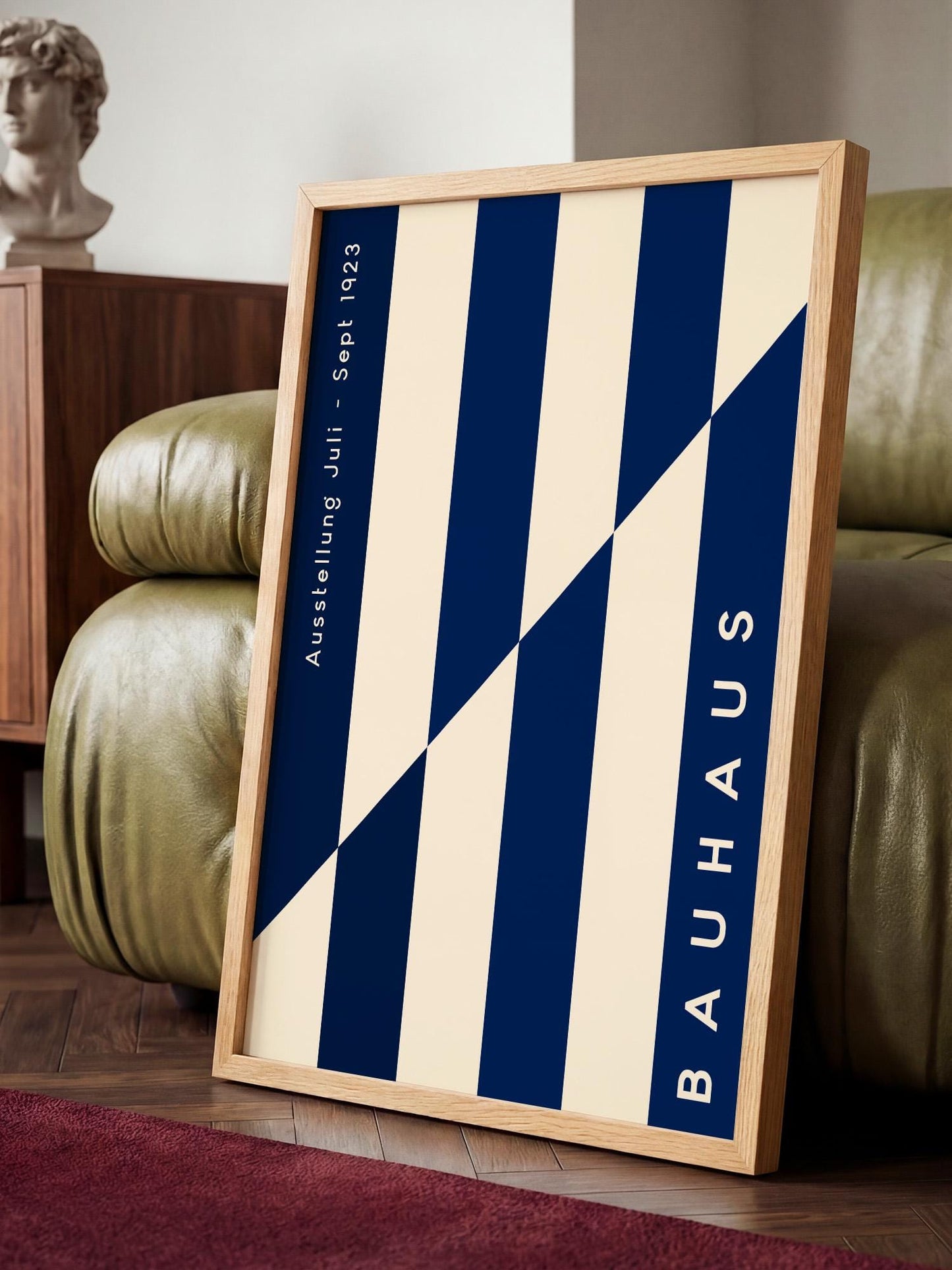 a framed poster of the Bauhaus design style, with a geometric pattern of blue and white stripes. The poster is placed on a wooden floor in front of a green leather couch.