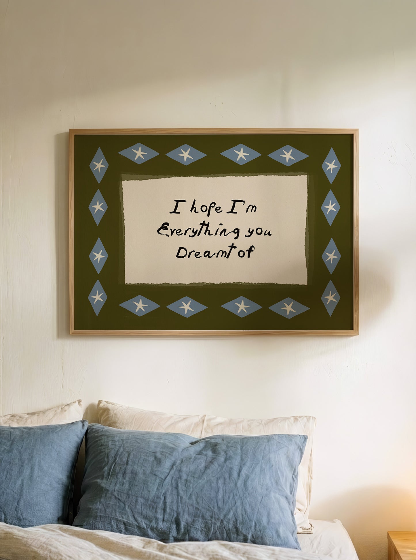 a framed piece of art hanging on a wall above a bed with blue pillows.