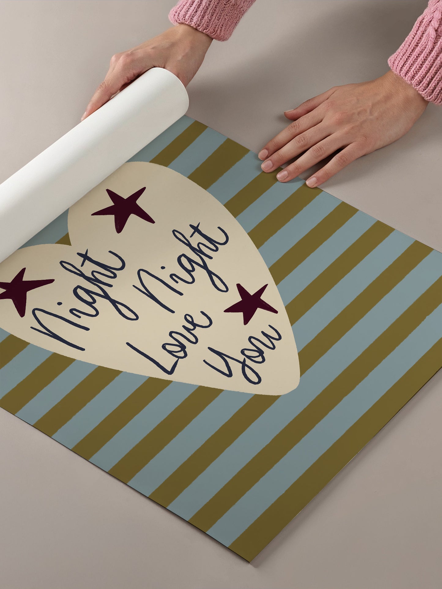 A person's hands are holding a roll of paper, which is placed on a striped paper with a heart-shaped design and stars.