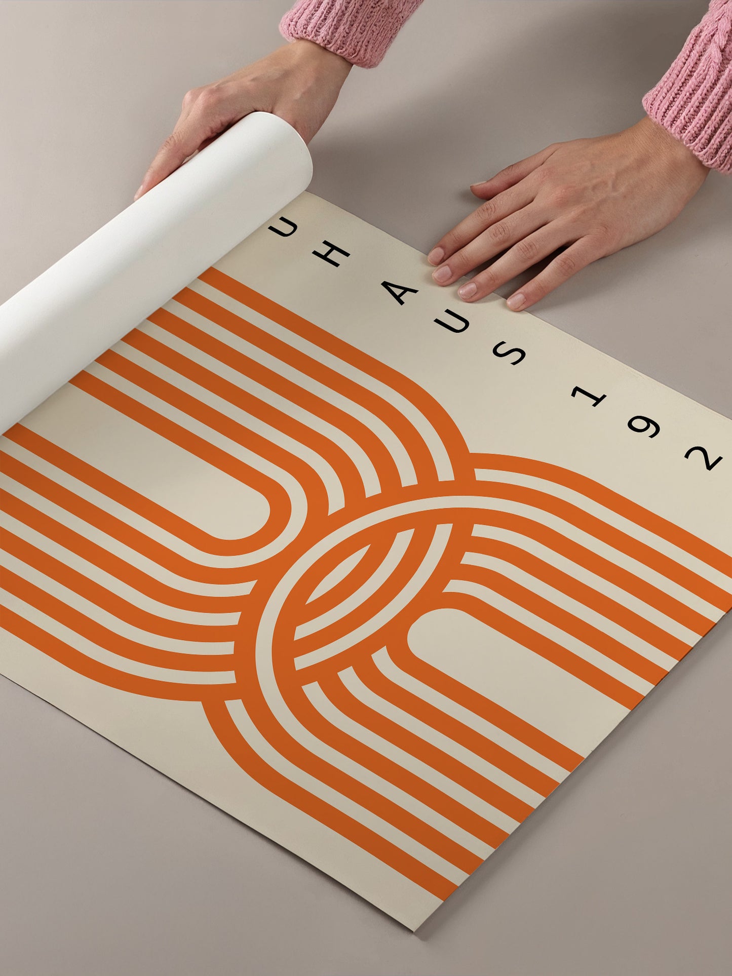 A person's hands are holding a roll of paper with a large, abstract orange and white design on it.