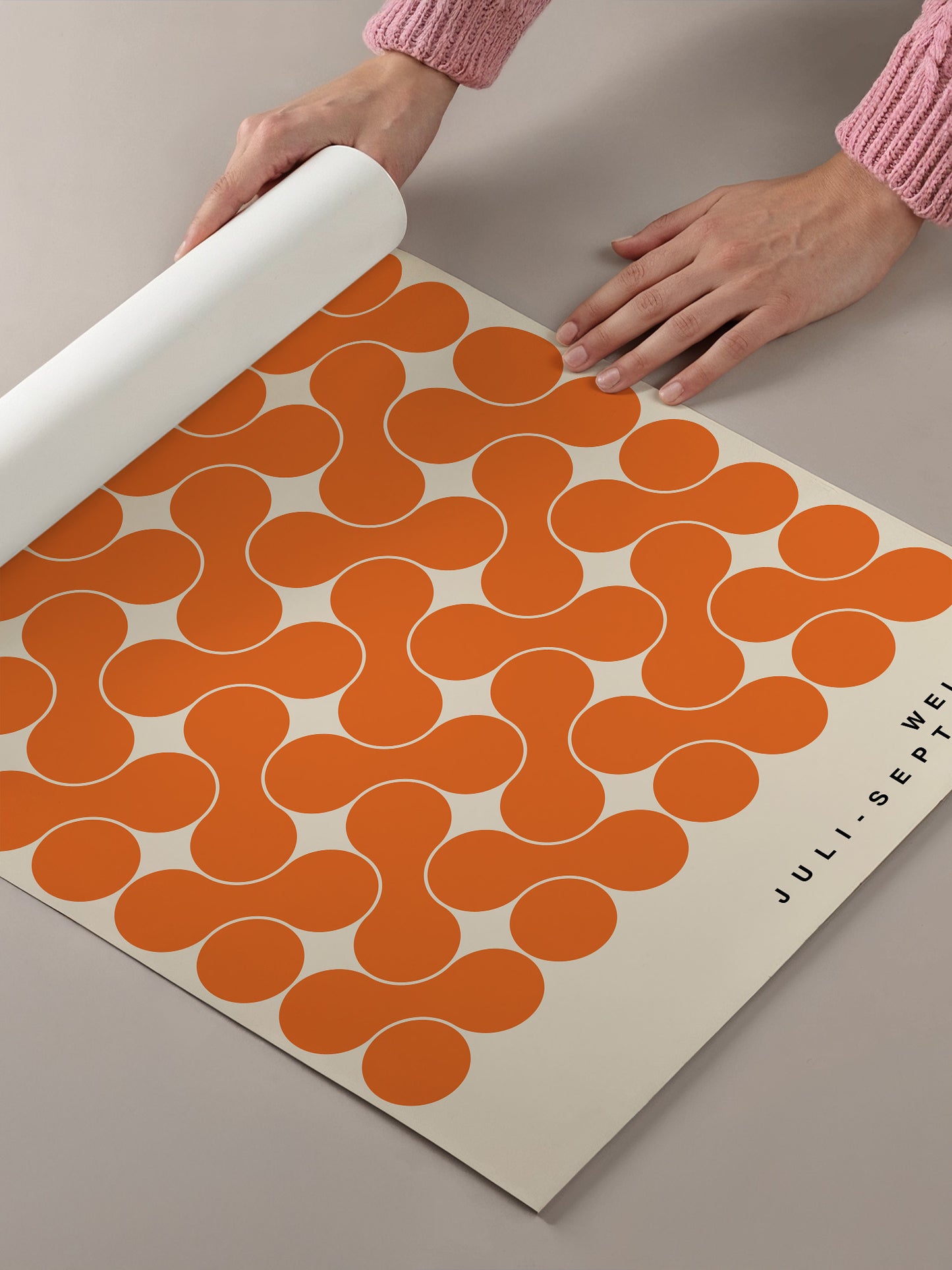 A person's hands are holding a roll of paper with a repeating pattern of orange circles on a beige background.
