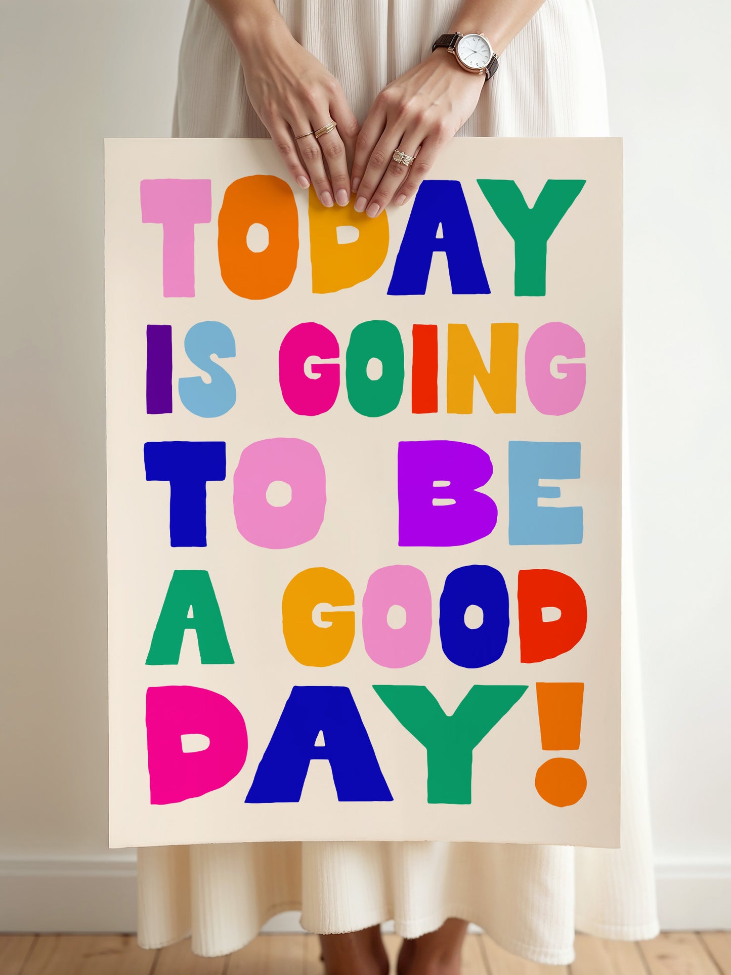 A person is holding a poster with the text "Today is going to be a good day!" written in a colorful, playful font.