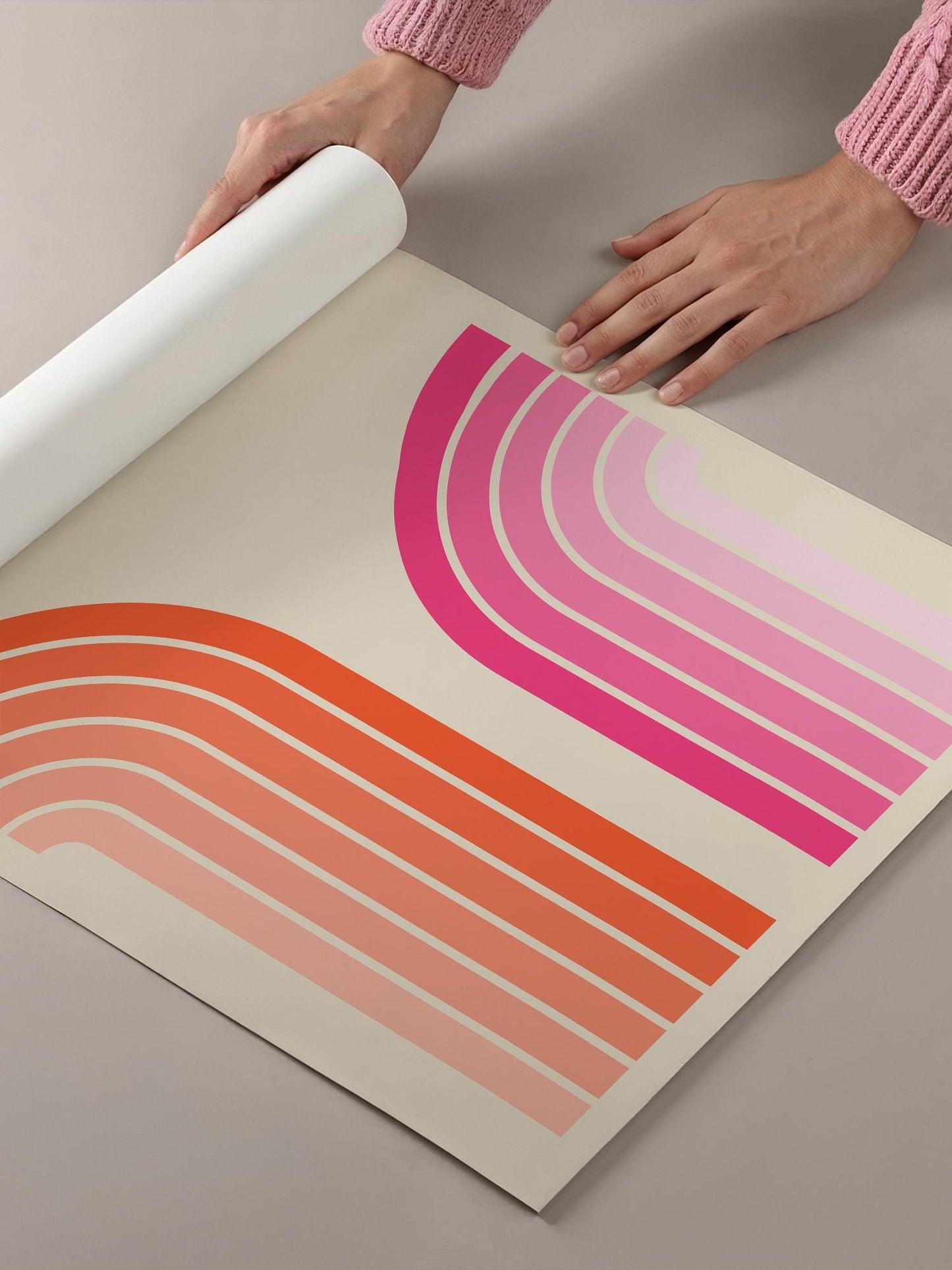 A person's hands are holding a roll of paper with a vibrant abstract design featuring curved lines in shades of pink and orange.