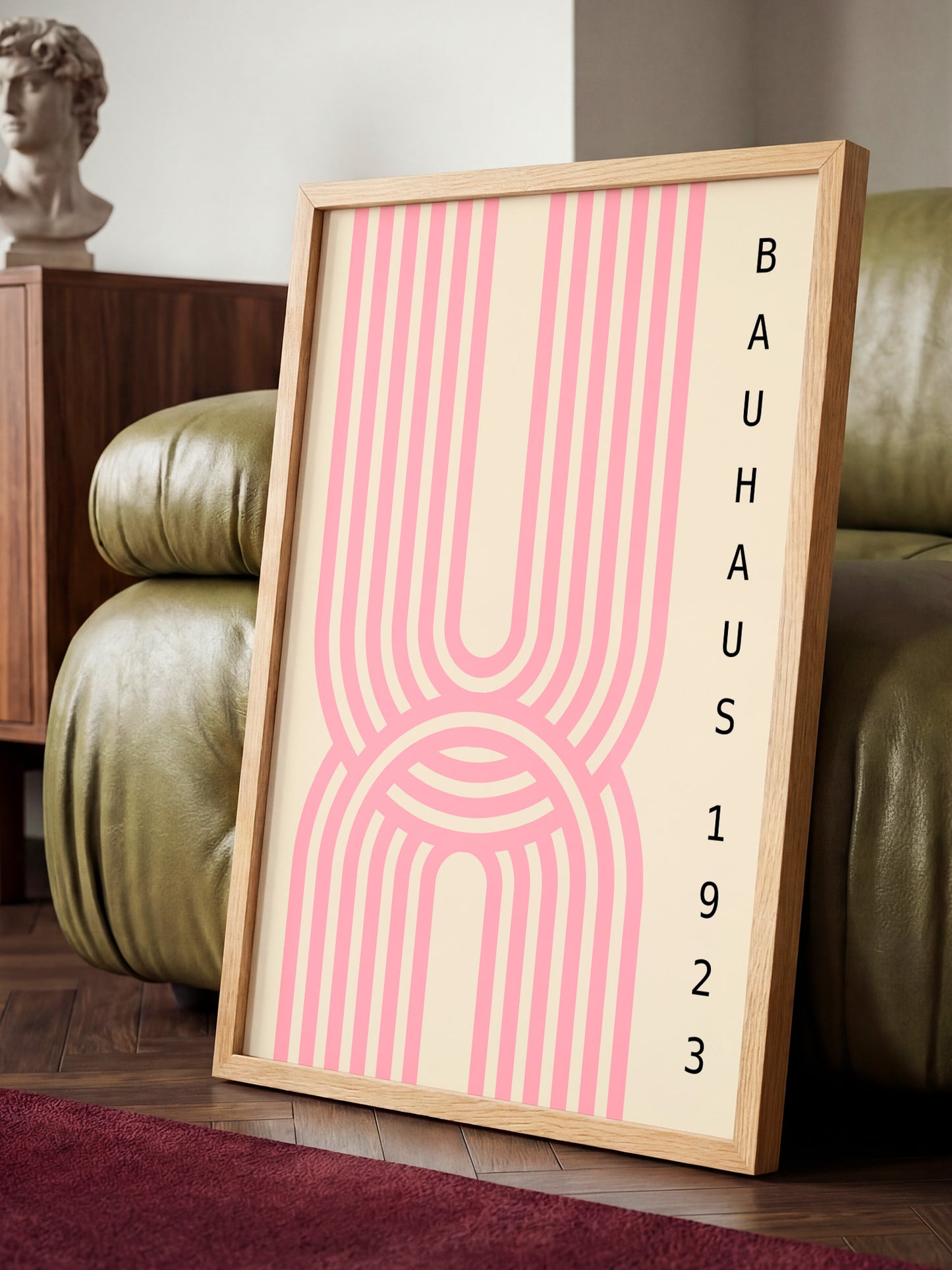 A framed poster with a pink and white striped design is displayed on a wooden floor in a room with a green leather couch.