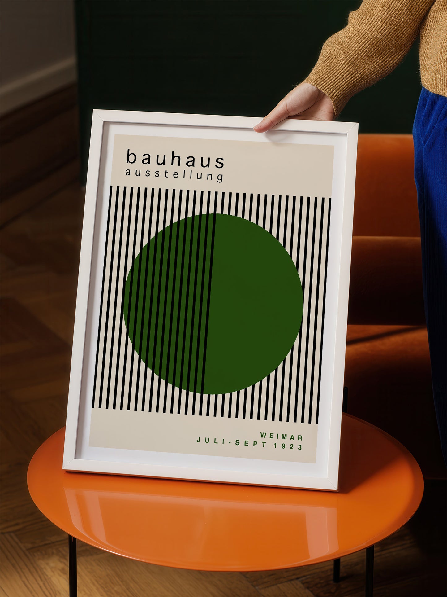 A person is holding a framed poster with a minimalist design featuring a green circle and black vertical lines.