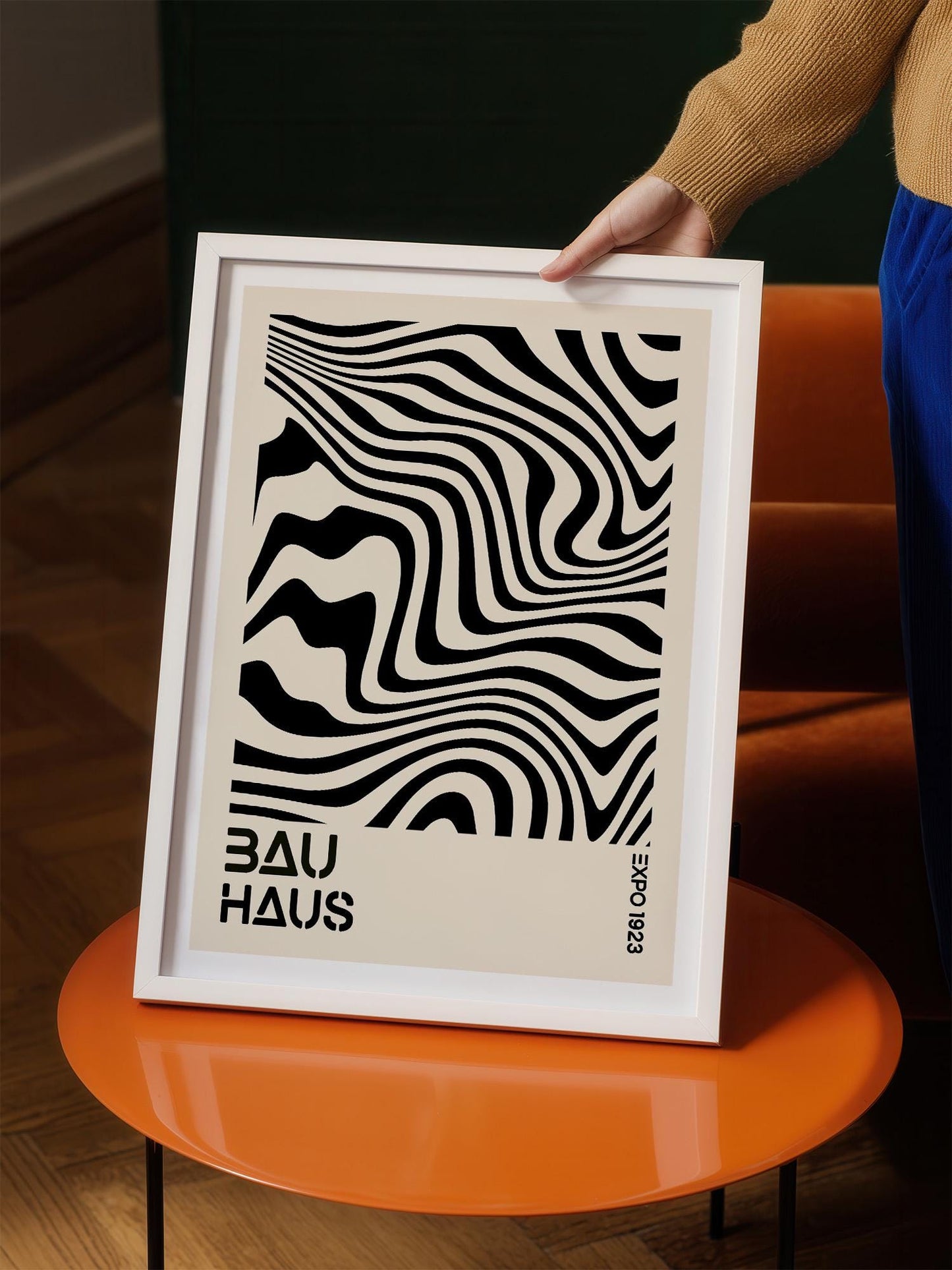 A person is holding a framed poster with a black and white abstract design featuring wavy lines.