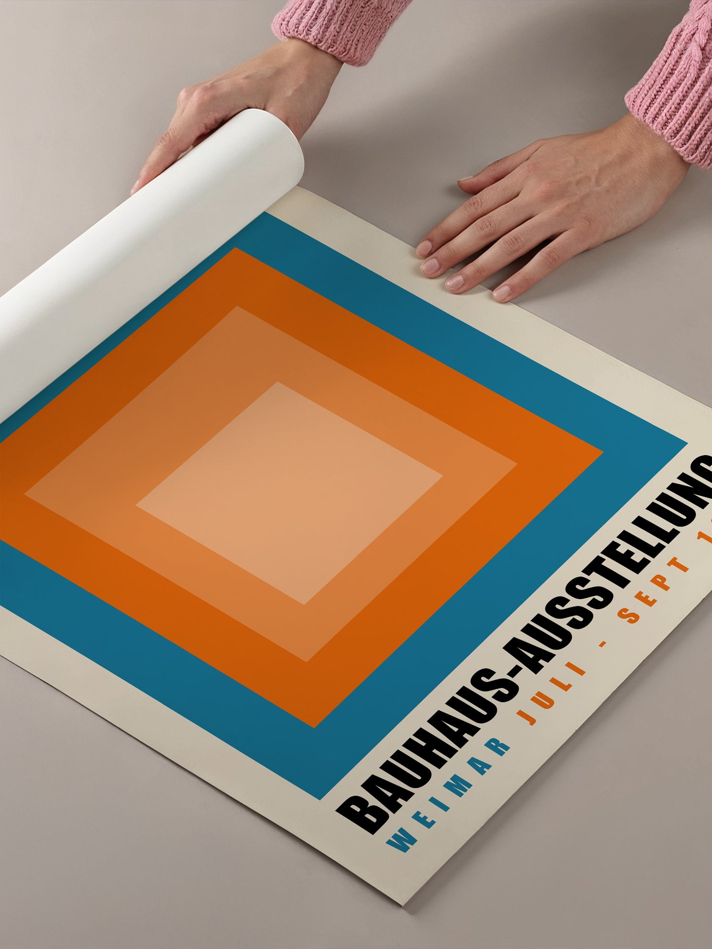 A person's hands are holding a roll of paper, which appears to be a poster or flyer for an event related to Bauhaus art.