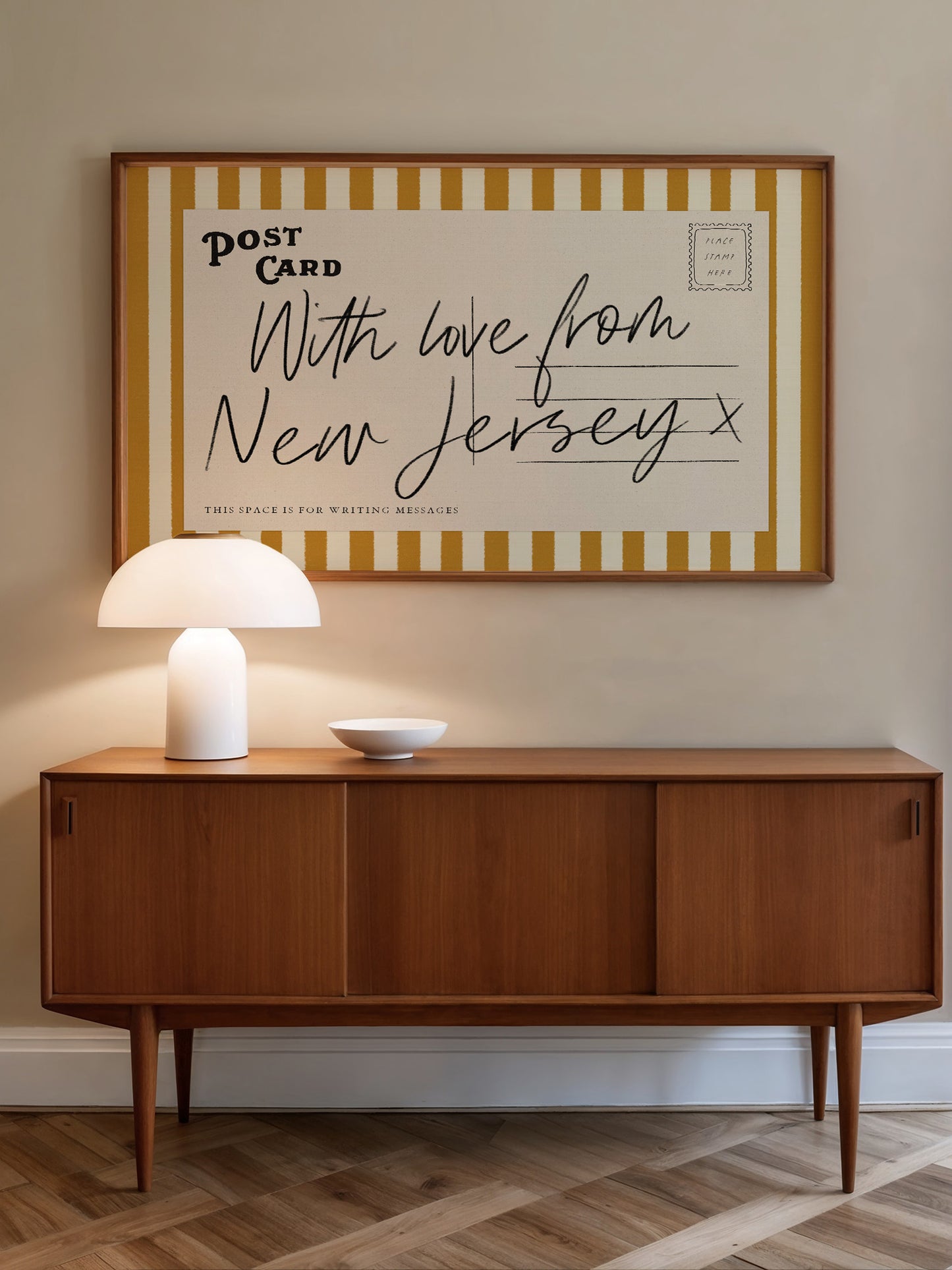 a wooden cabinet with a white lamp on top, and a framed poster with a handwritten message hanging on the wall above it.