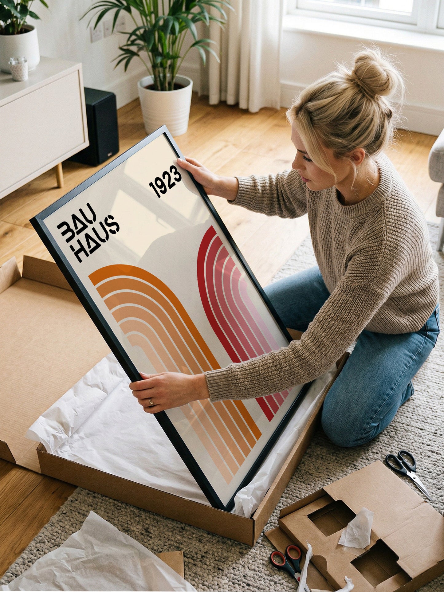 A woman is kneeling on the floor and holding a framed poster with the text "Bauhaus 1923" on it.