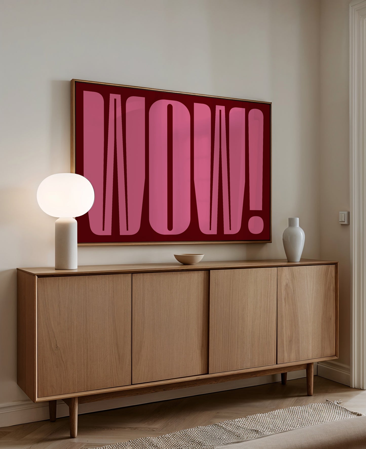a wooden cabinet with a large pink graphic on the wall above it, and a white lamp on the cabinet.