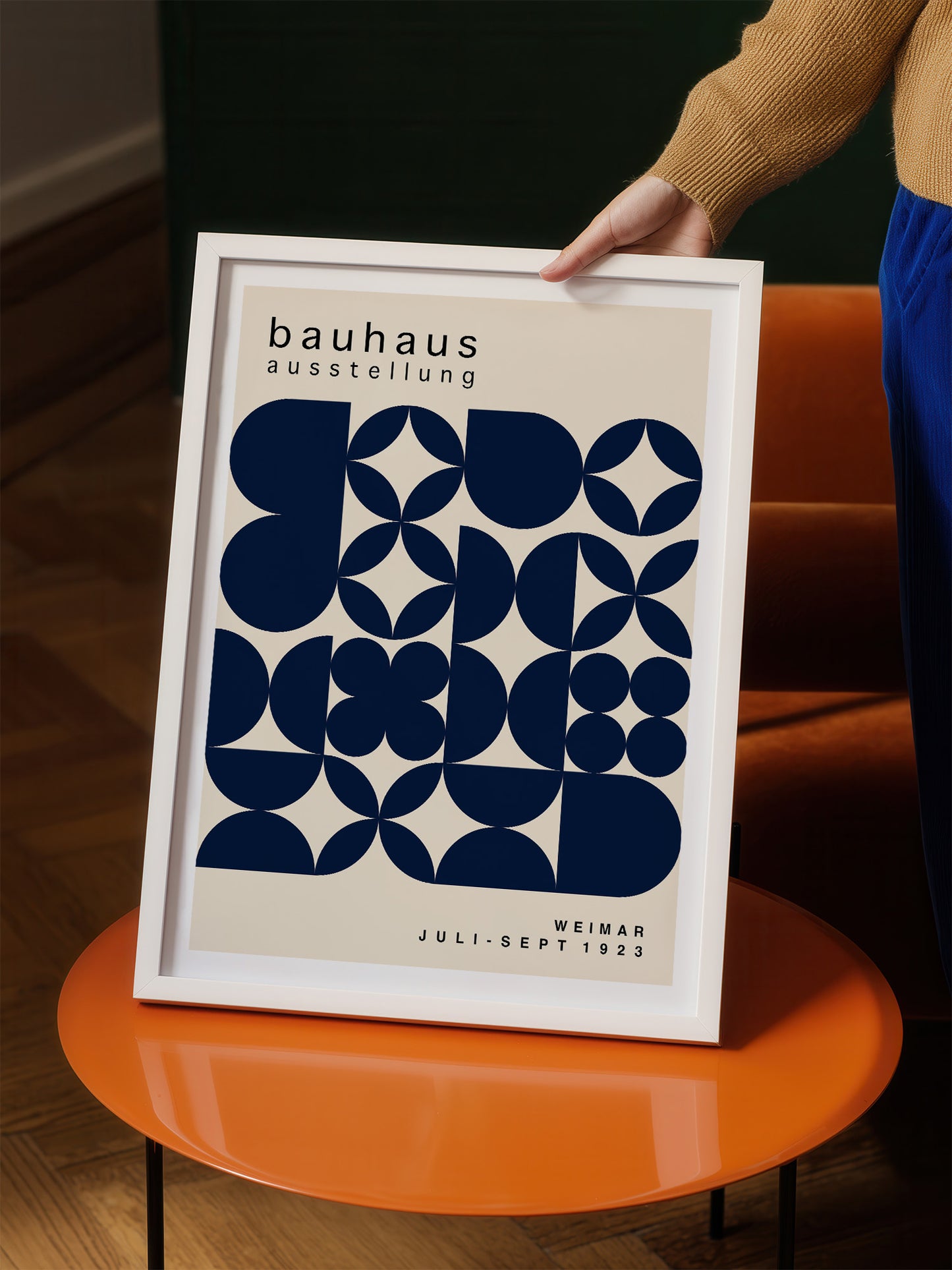 A person is holding up a framed poster with a geometric design in shades of blue and white.