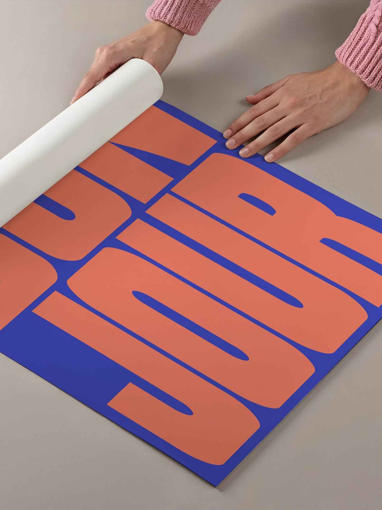 A person's hands are holding a roll of paper, which is placed on top of a large poster with bold, orange and blue text.