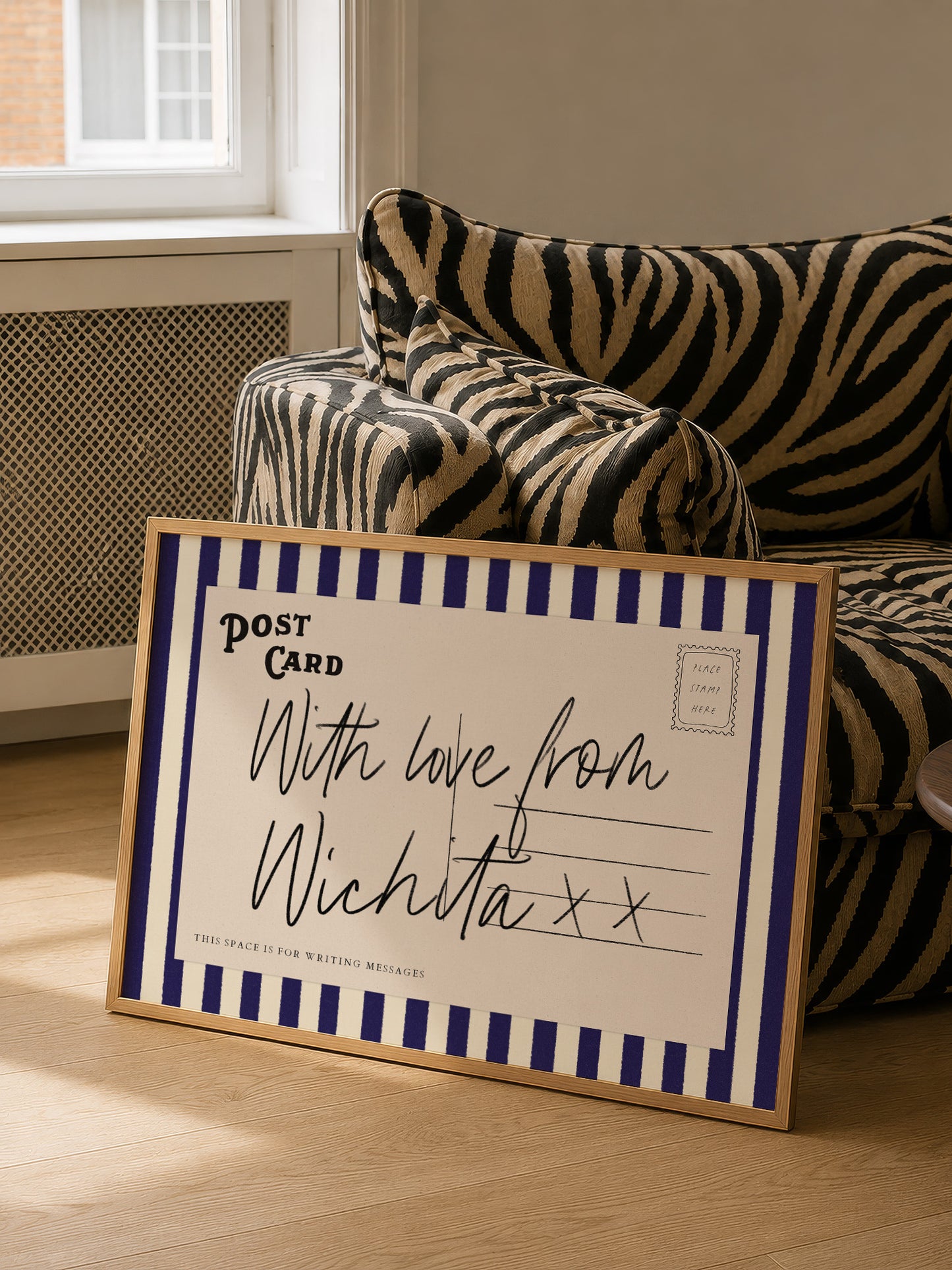 A framed postcard with a handwritten message is placed on a couch in a room.