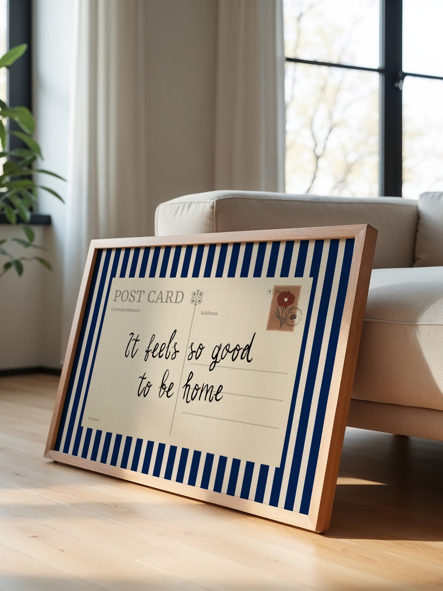 A framed postcard with a handwritten message is leaning against a white couch in a room with a window.