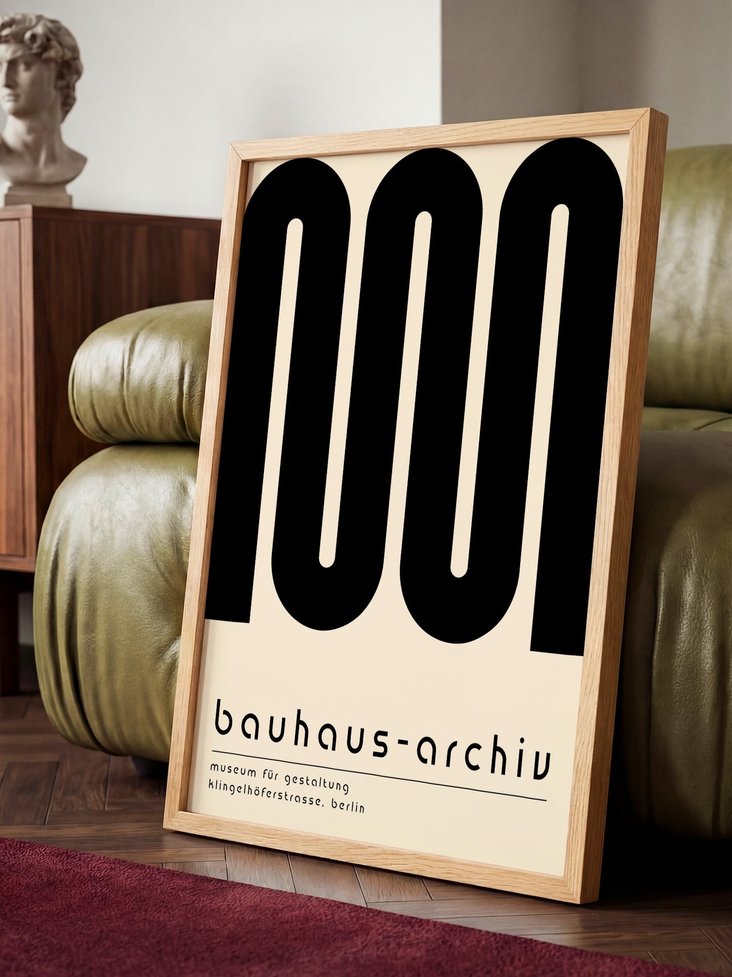 a large poster with the text "bauhaus-archivu" and "museum für gestaltung, künigkeitfürstärze, berlin" on it, placed on a wooden floor in front of a green leather couch.