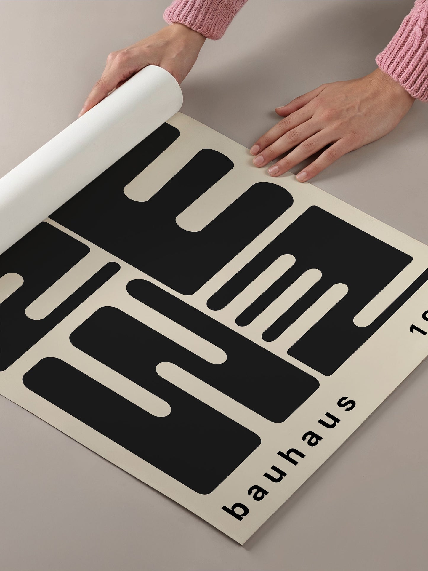 A person's hands are holding a roll of paper, which appears to be a poster or artwork featuring a large black and white geometric design.