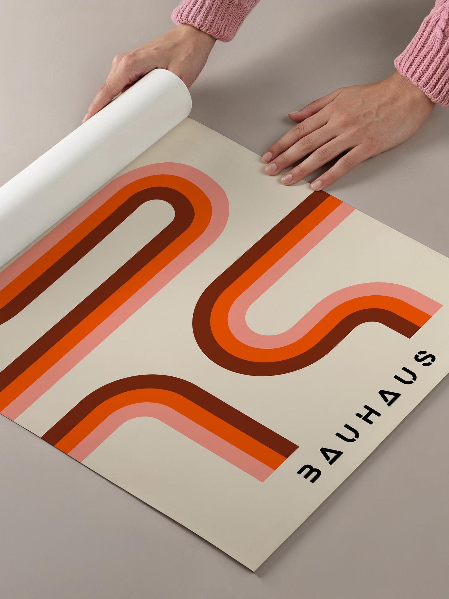 A person's hands are holding a roll of paper with a large, abstract design featuring curved lines in shades of orange and pink.