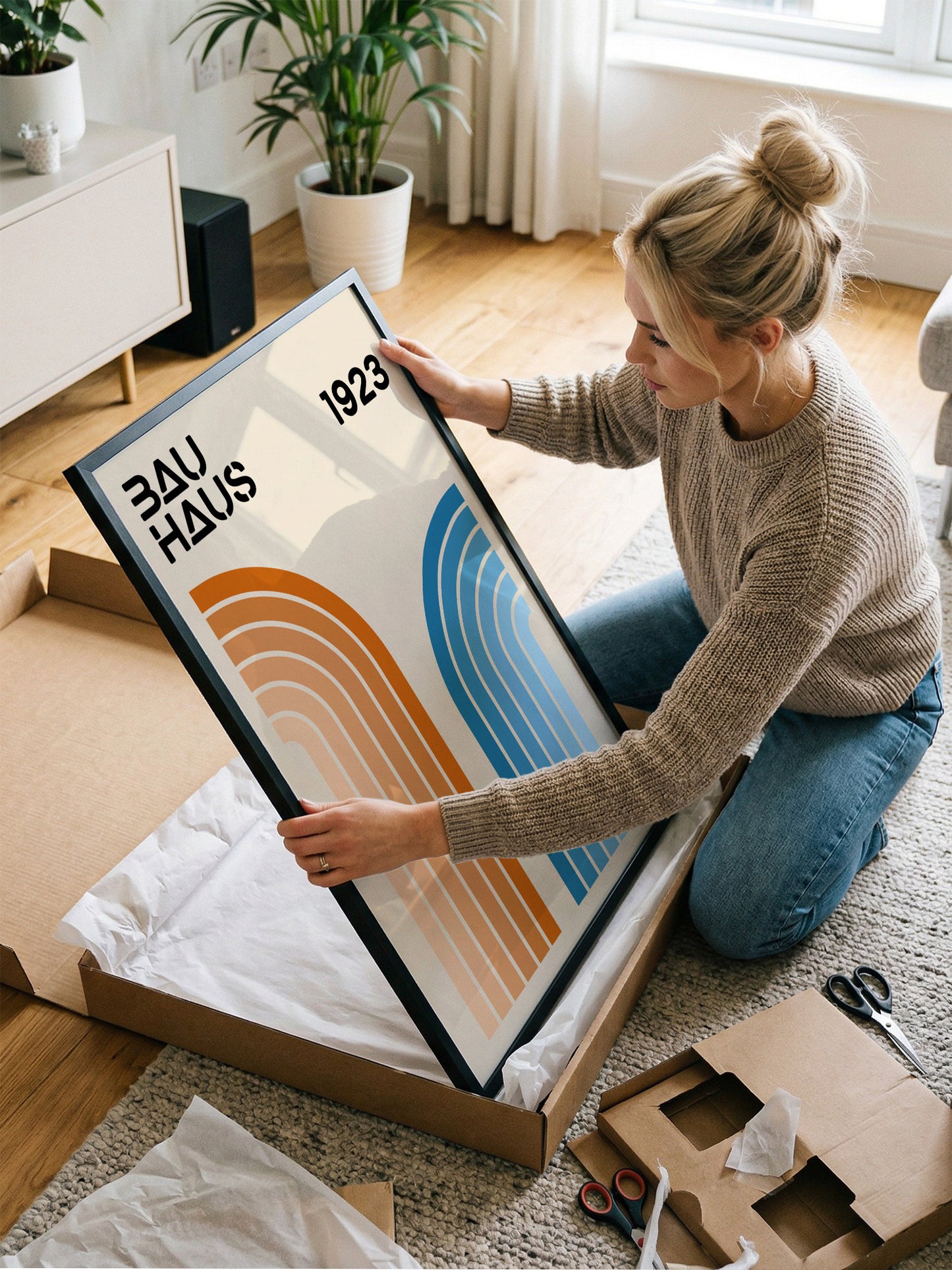 A woman is kneeling on the floor and holding a framed poster with the text "Bauhaus 1923" on it.