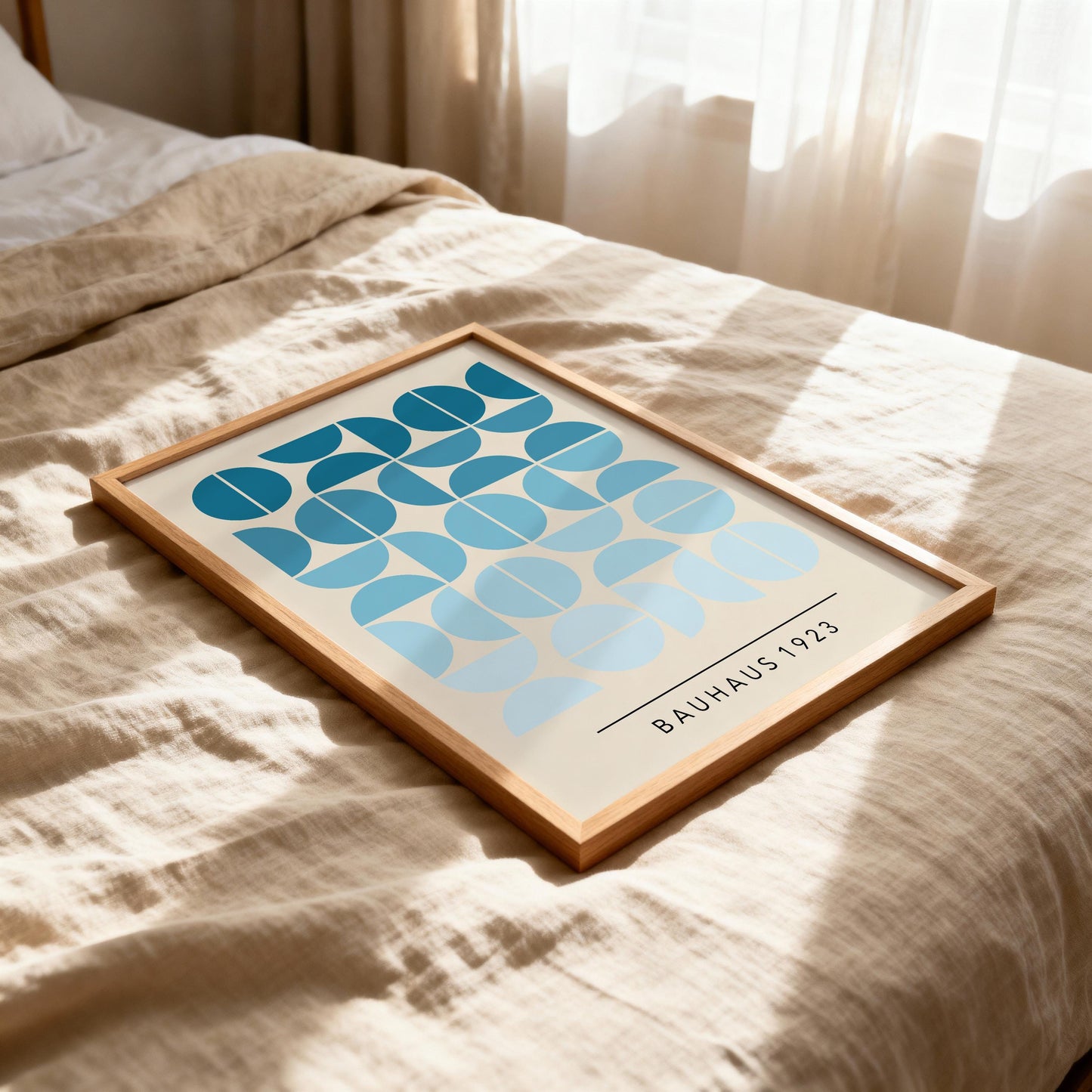 a framed print of a geometric design with blue and white shapes, placed on a bed with a beige blanket.