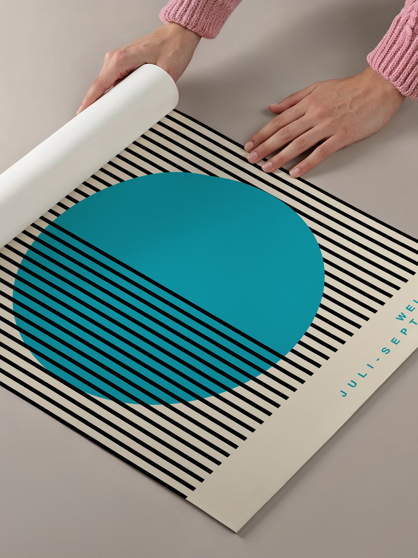 A person's hands are holding a roll of paper, which appears to be a poster or artwork with a large blue circle and black and white striped background.