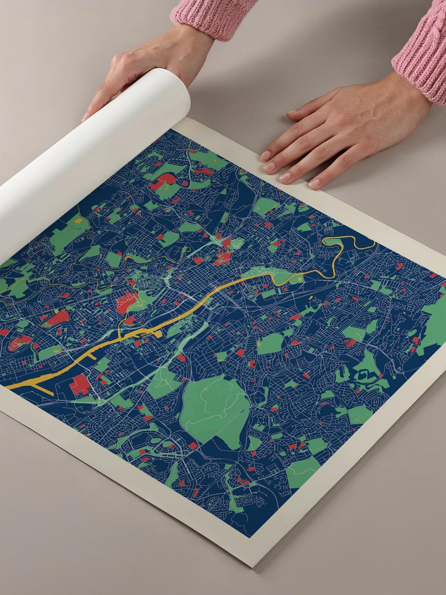 A person's hands are holding a roll of paper over a colorful map of a city, which appears to be a detailed and vibrant representation of the urban landscape.