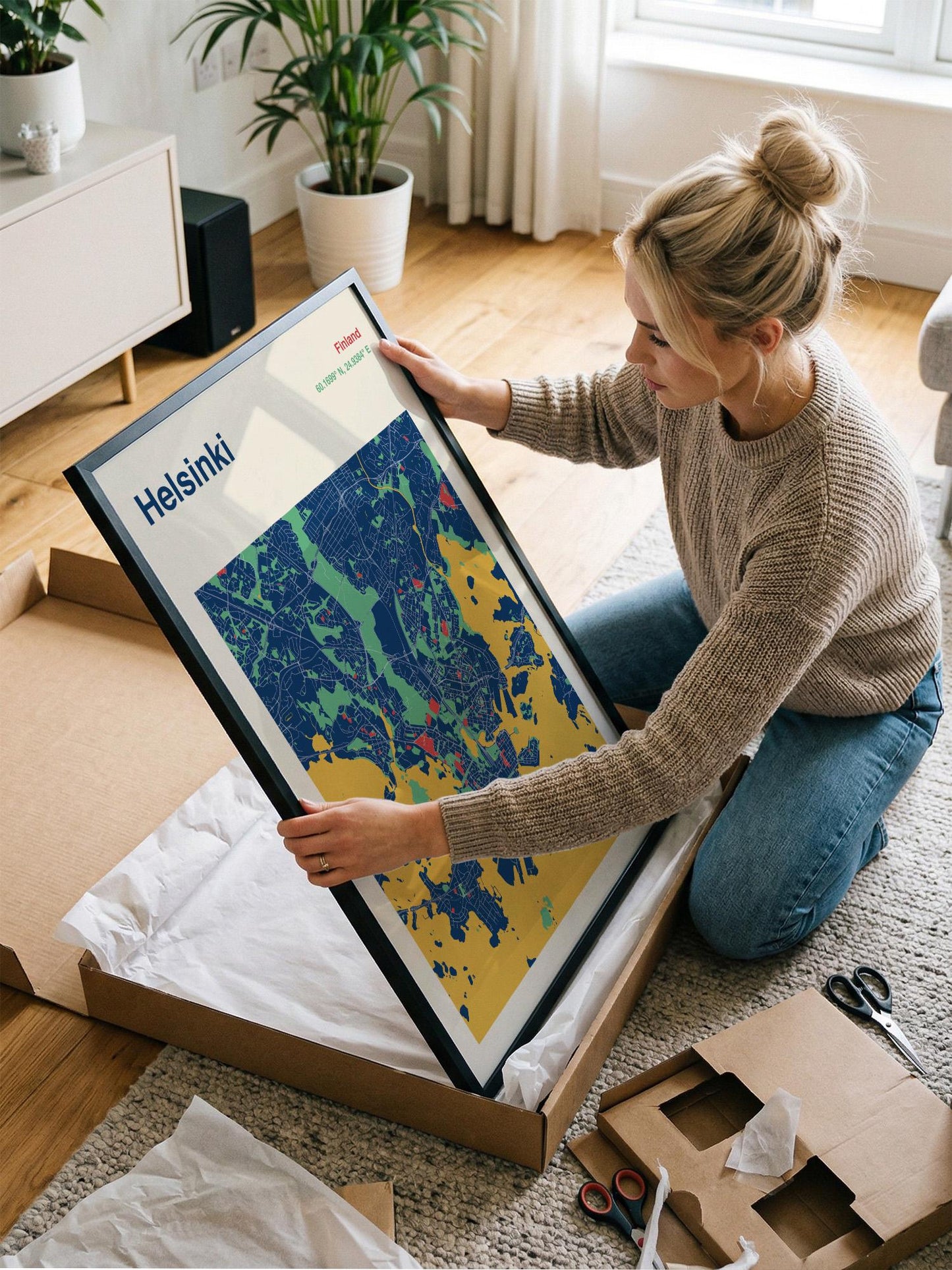 A woman is kneeling on the floor and holding a framed map of Helsinki, Finland.
