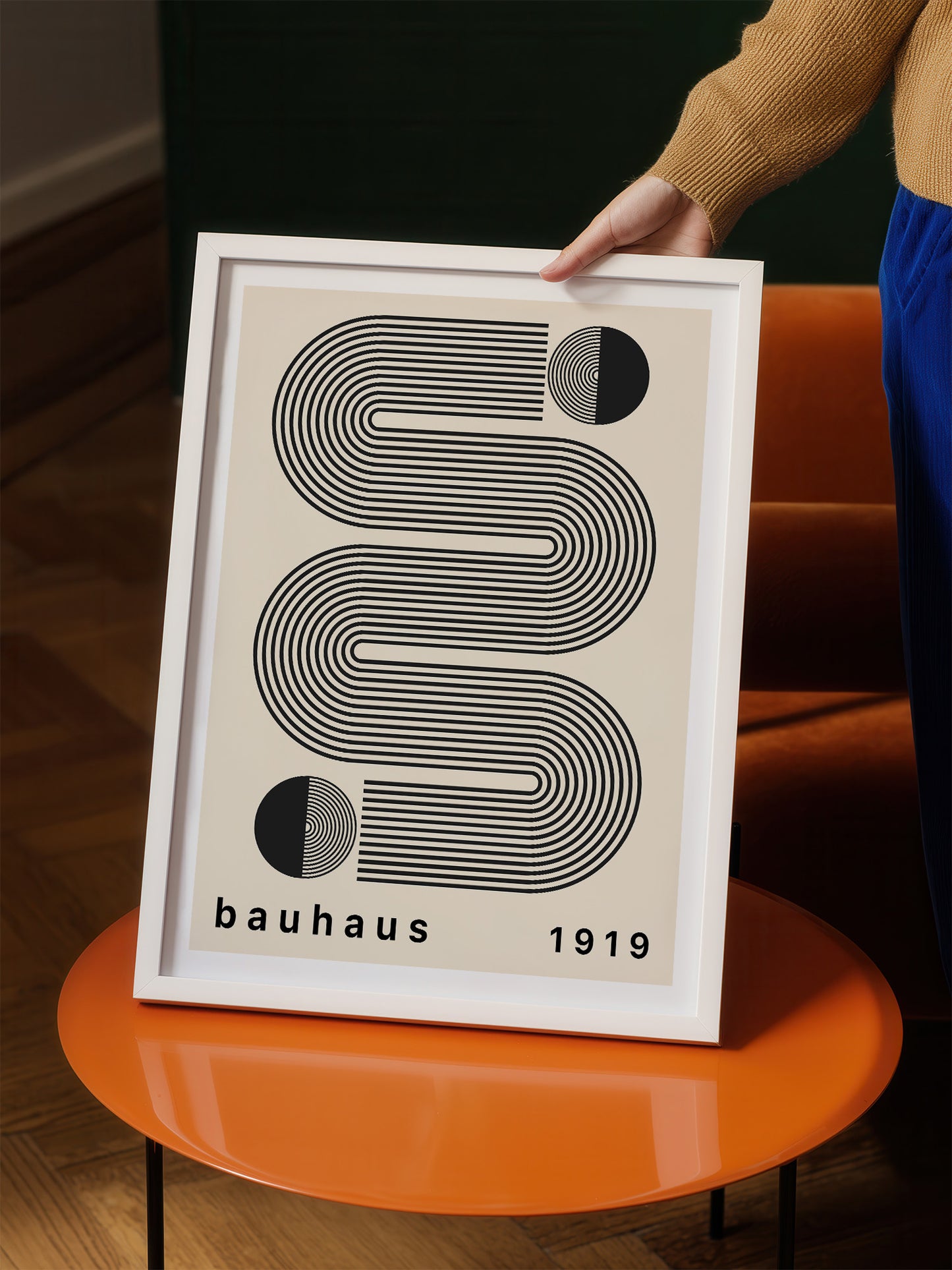 A person is holding up a framed poster with a minimalist design featuring a series of curved lines and circles.