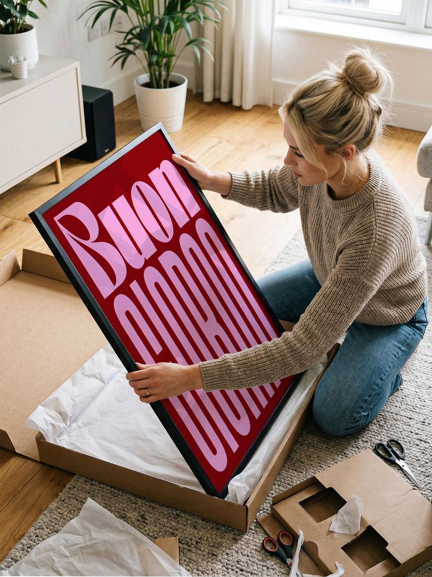 A woman is kneeling on the floor and holding a large framed poster with the text "Buon promovi" on it.